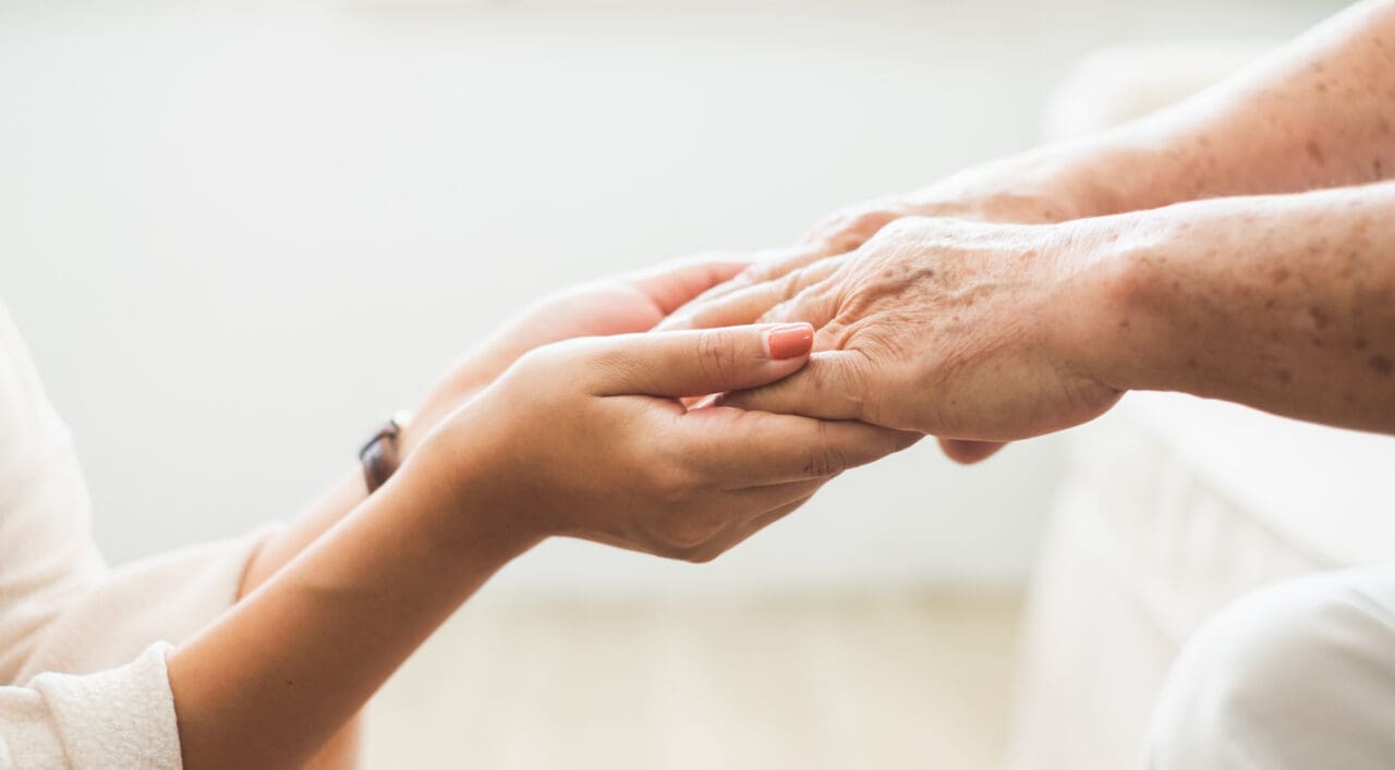 A person gently holding the hands of an elderly individual, symbolizing care and support in a healthcare setting.