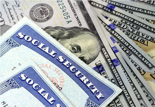 A close-up of U.S. paper currency, including Social Security cards and various denominations of dollar bills, with part of a Social Security badge visible in the background.